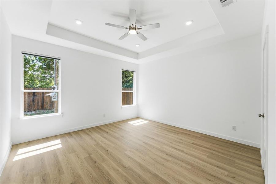 Spacious room featuring wood-finish flooring, a tray ceiling with recessed lighting, and a ceiling fan with integrated lighting