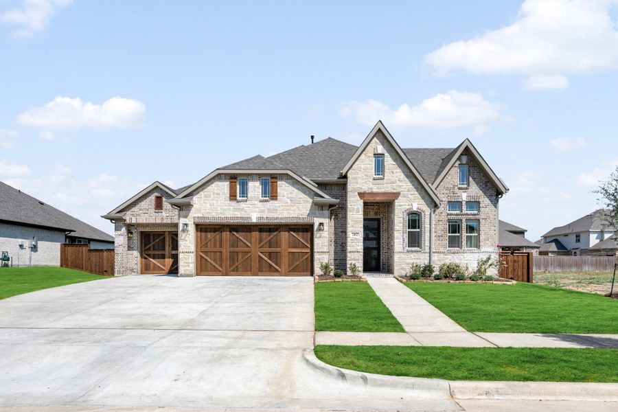 Single-story home with stone and brick exterior, three-car garage with wood doors, and green front lawn. Single-story home with stone and brick exterior, three-car garage with wood doors, and green front lawn.