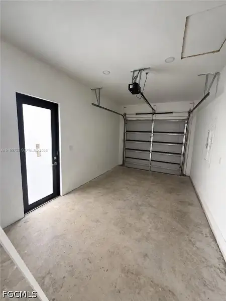 Enclosed garage featuring concrete flooring, white walls, recessed ceiling lighting, and a side-entry door with a black frame