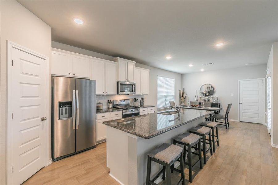 Kitchen featuring stainless steel appliances, dark stone counters, backsplash, a breakfast bar area, and light wood-style floors