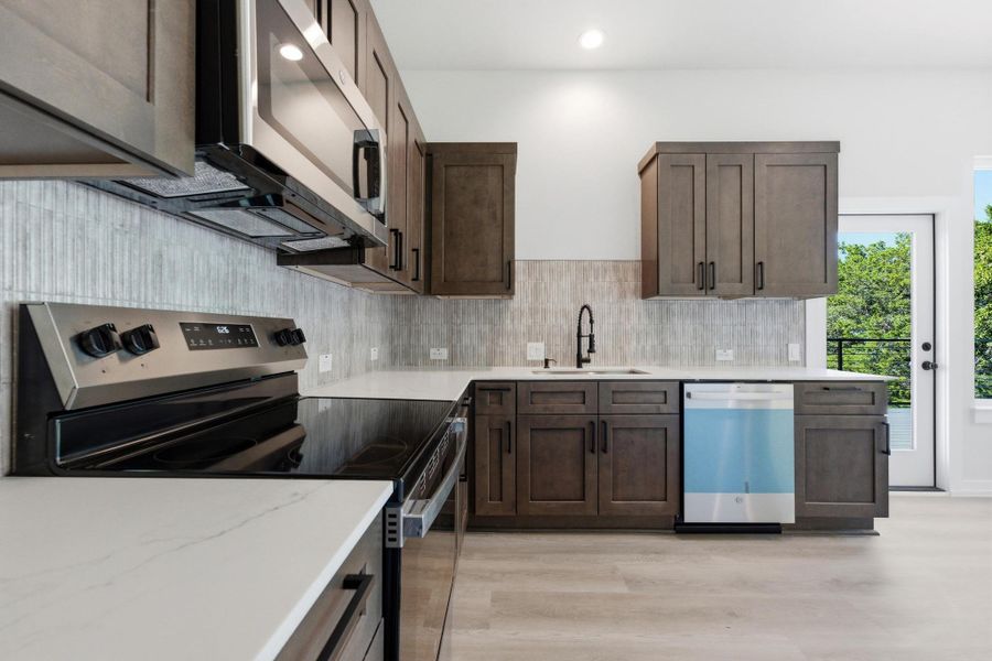 Kitchen with stainless steel appliances, dark brown cabinets, light stone countertops, tasteful backsplash, and light wood-type flooring