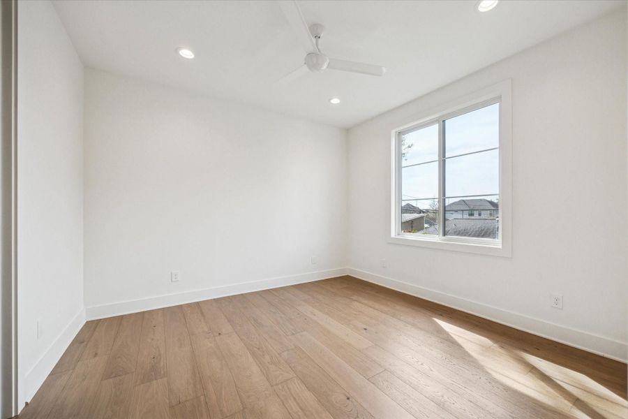 Light filled secondary bedroom features wide plank hardwood floors, recessed lighting, and a generously sized window overlooking the neighborhood. Clean lines and neutral finishes create a flexible space ready for guests, a nursery, or a dedicated home office.