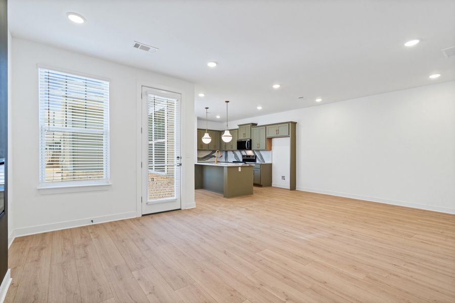 Open-concept living area featuring light wood-finish flooring, recessed lighting, and a white color palette Open-concept living area featuring light wood-finish flooring, recessed lighting, and a white color palette