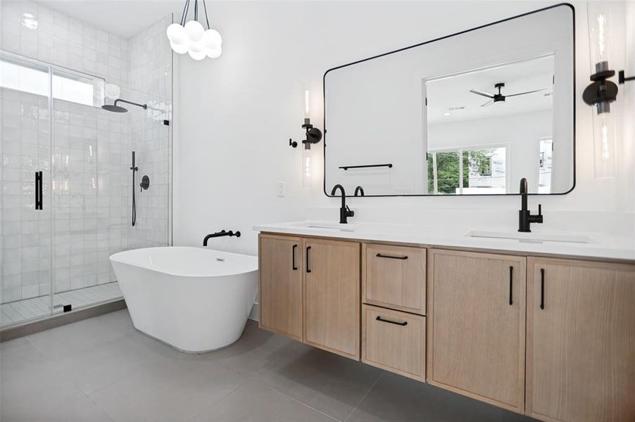 Modern bathroom featuring a freestanding soaking tub, glass-enclosed shower with subway tile surround, a dual vanity with light wood-finish cabinetry, a large framed mirror, and matte black fixtures throughout