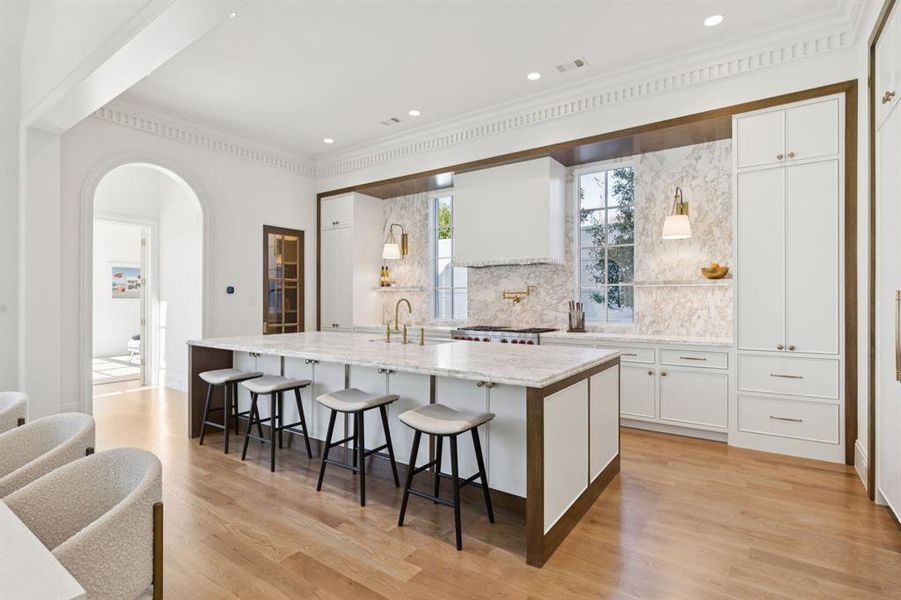 Kitchen featuring white cabinetry, a breakfast bar area, a large island with sink, light stone countertops, and crown molding