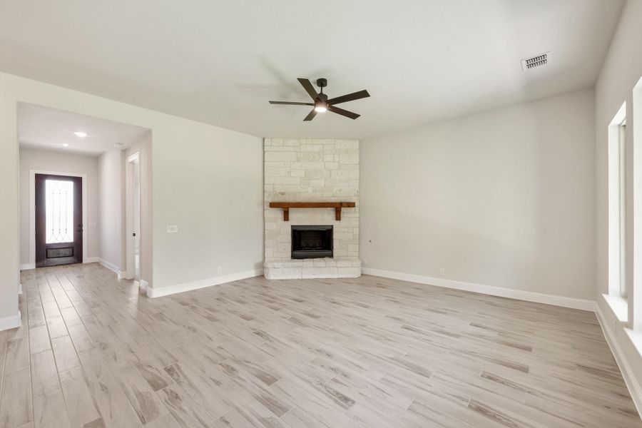 Empty living room with light wood floors, stone fireplace with wood mantel, and ceiling fan