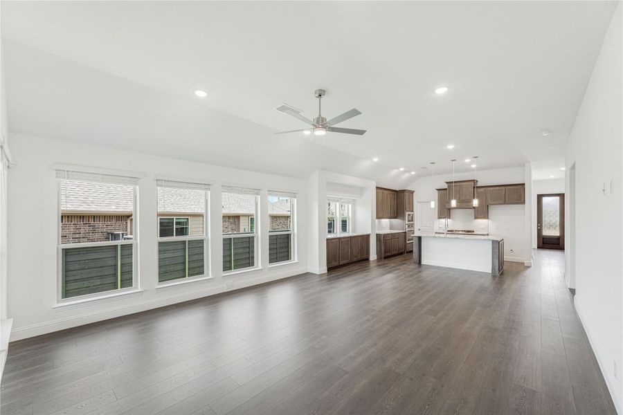 Open living area with dark hardwood floors, ceiling fan, and kitchen with dark wood cabinets in background Open living area with dark hardwood floors, ceiling fan, and kitchen with dark wood cabinets in background