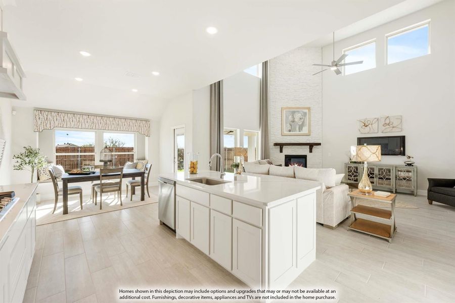 Open-concept kitchen with white island and sink, flowing into dining and living areas with high ceilings and fireplace.
