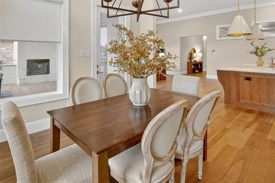 Dining space featuring light wood-type flooring, crown molding, a fireplace with raised hearth, a chandelier, and recessed lighting