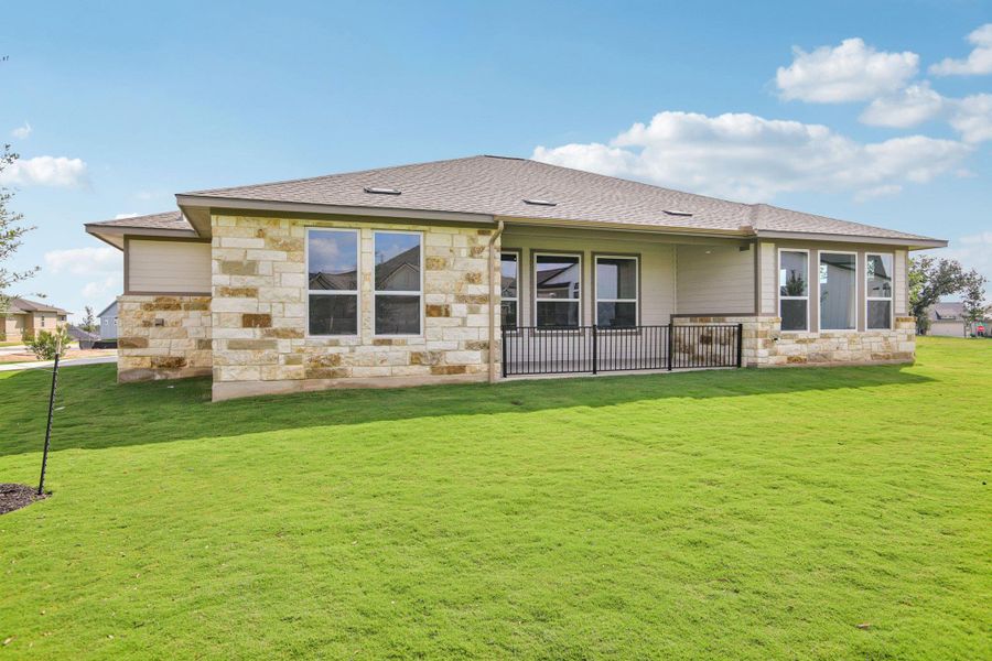 Back of house featuring stone siding, a yard, roof with shingles, and a patio area