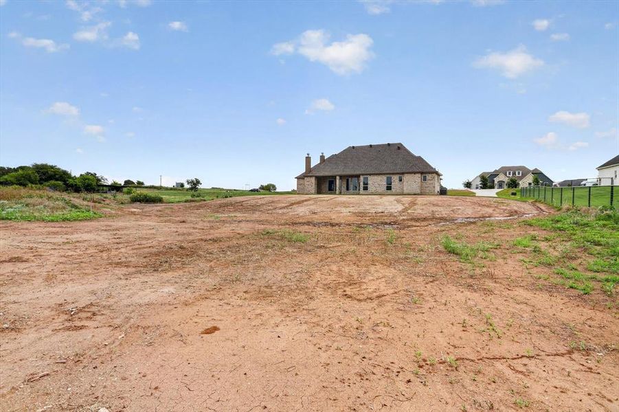 Large undeveloped lot featuring exposed earth, distant residential structures, and a partial perimeter fence Large undeveloped lot featuring exposed earth, distant residential structures, and a partial perimeter fence
