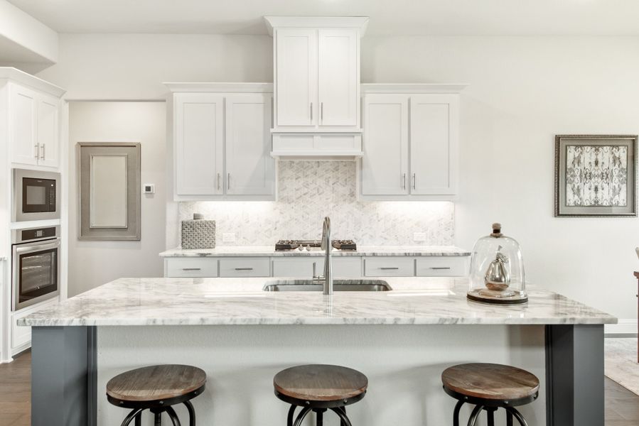Kitchen with white cabinets, marble countertop island with sink, three bar stools, and stainless steel appliances