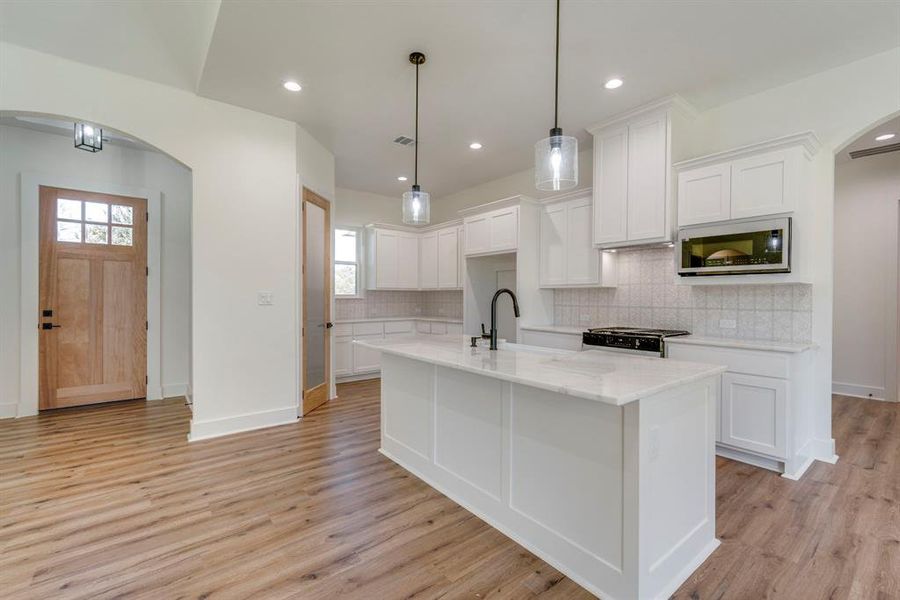 Kitchen with white cabinetry, stove, and hanging light fixtures