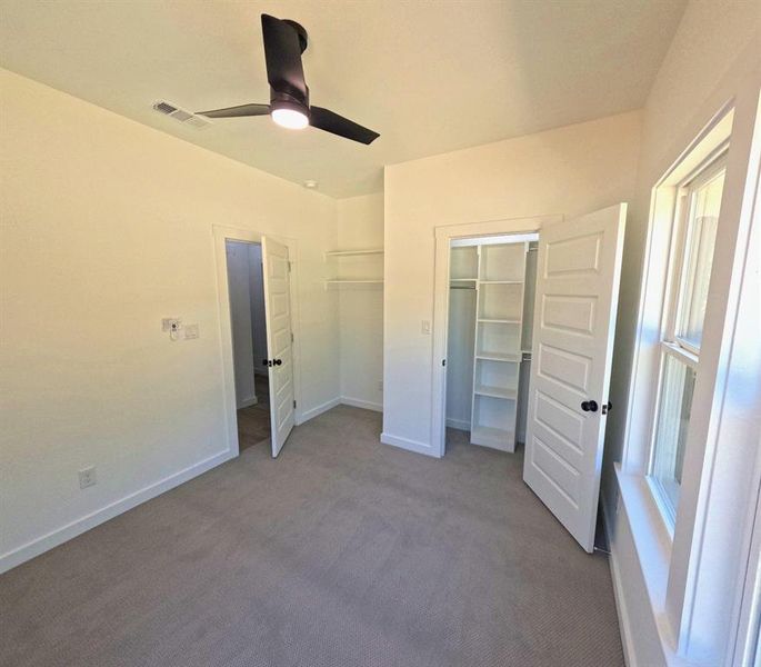 Unfurnished bedroom featuring dark colored carpet, ceiling fan, and a walk in closet Unfurnished bedroom featuring dark colored carpet, ceiling fan, and a walk in closet