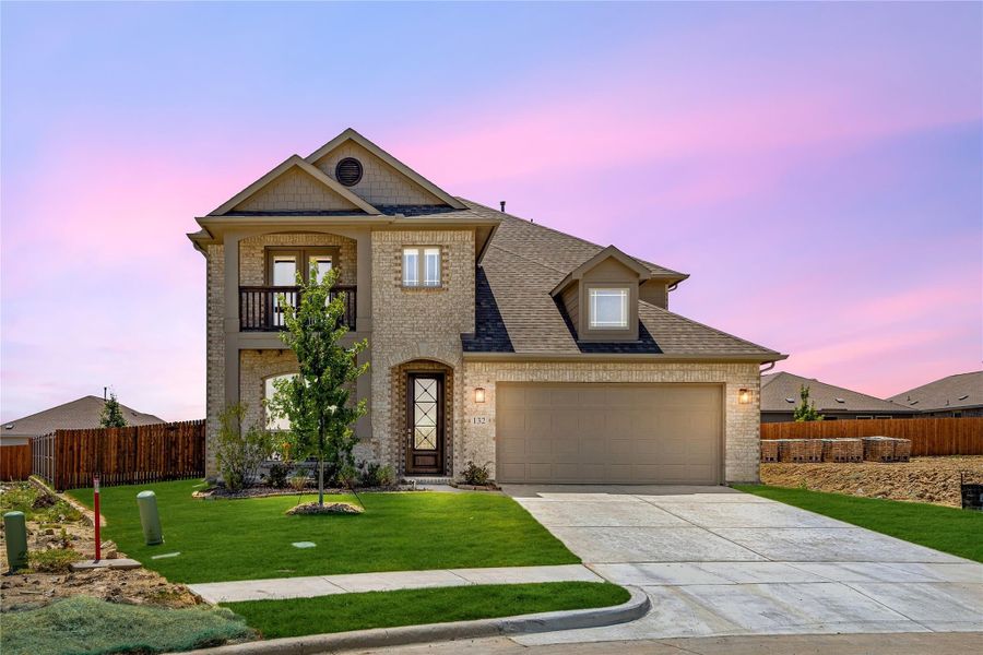 Two-story brick home with arched entry, second-floor balcony, two-car garage, and manicured front lawn at dusk
