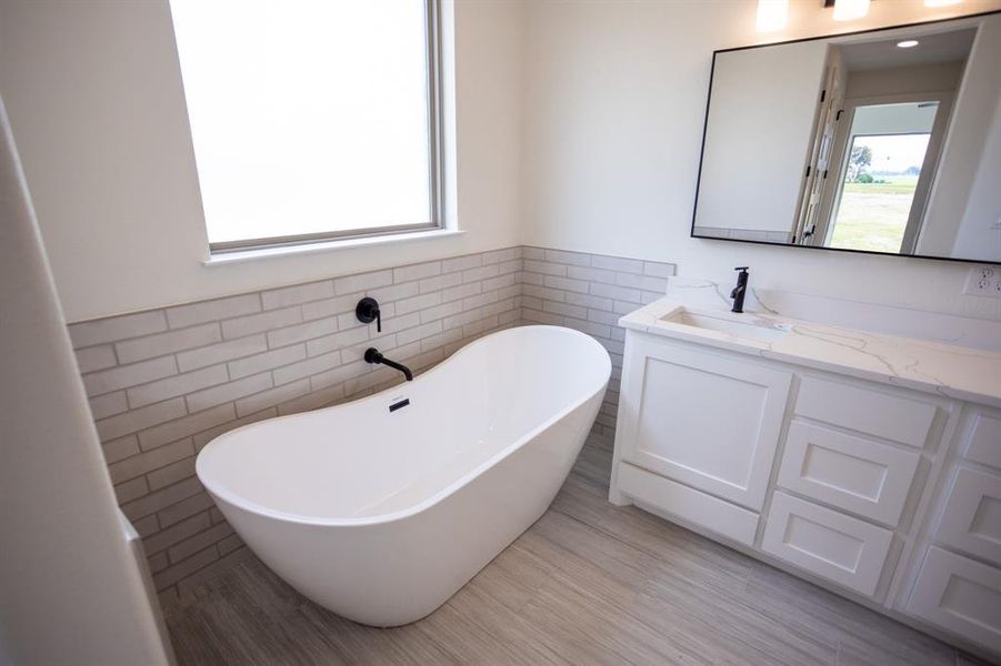 Bathroom featuring tile walls, a soaking tub, vanity, and wainscoting Bathroom featuring tile walls, a soaking tub, vanity, and wainscoting