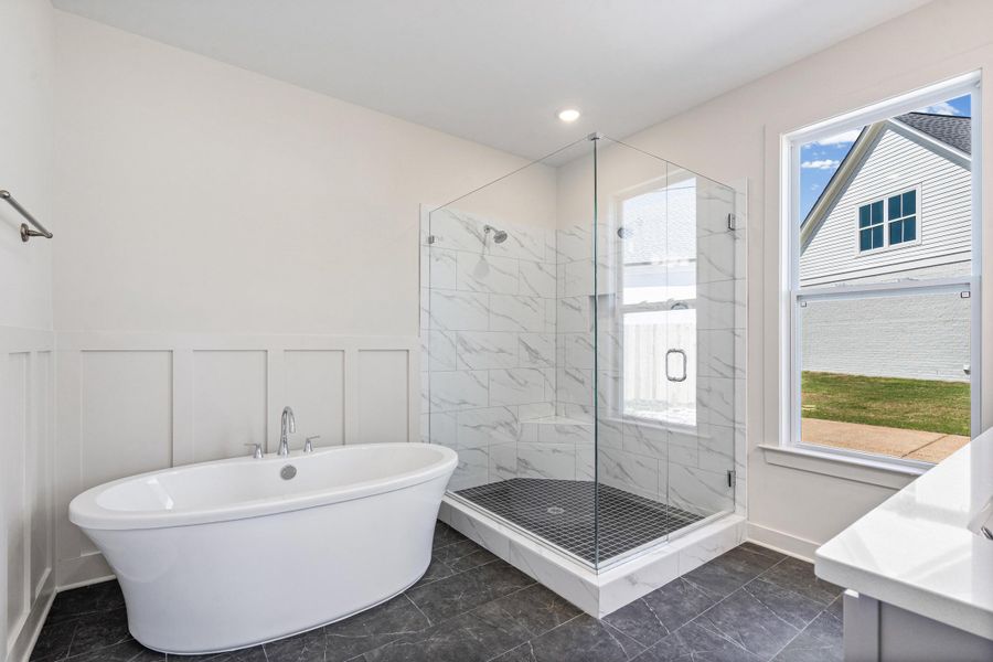 Bathroom with a marble finish shower, a freestanding tub, wainscoting, a decorative wall, and healthy amount of natural light