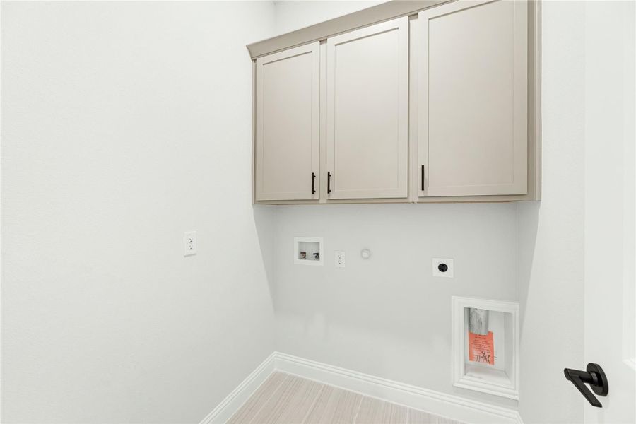 Laundry room with gray upper cabinets, washer and dryer hookups, and light wood-look flooring