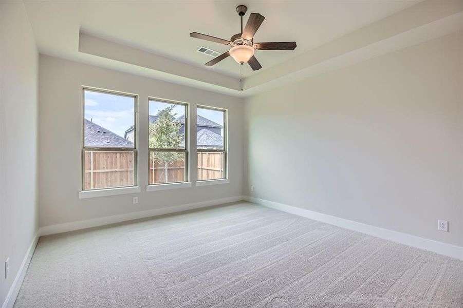 Carpeted empty room featuring a raised ceiling and ceiling fan