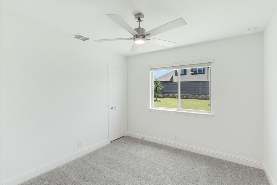 Empty bedroom with gray carpet, ceiling fan, and window overlooking backyard fence Empty bedroom with gray carpet, ceiling fan, and window overlooking backyard fence
