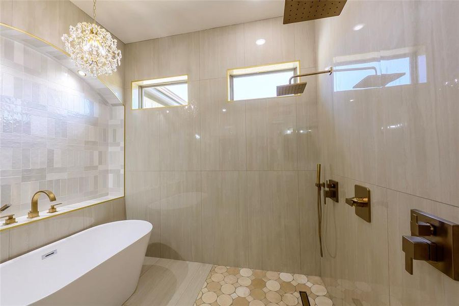 Full bath with tile walls, a walk in shower, a freestanding bath, and suspended lighting