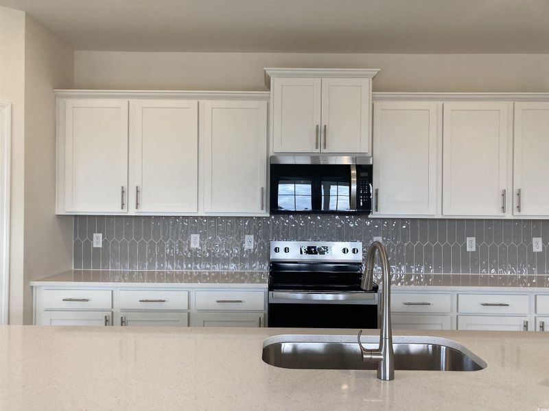Kitchen featuring white cabinetry, appliances with stainless steel finishes, light stone countertops, and backsplash
