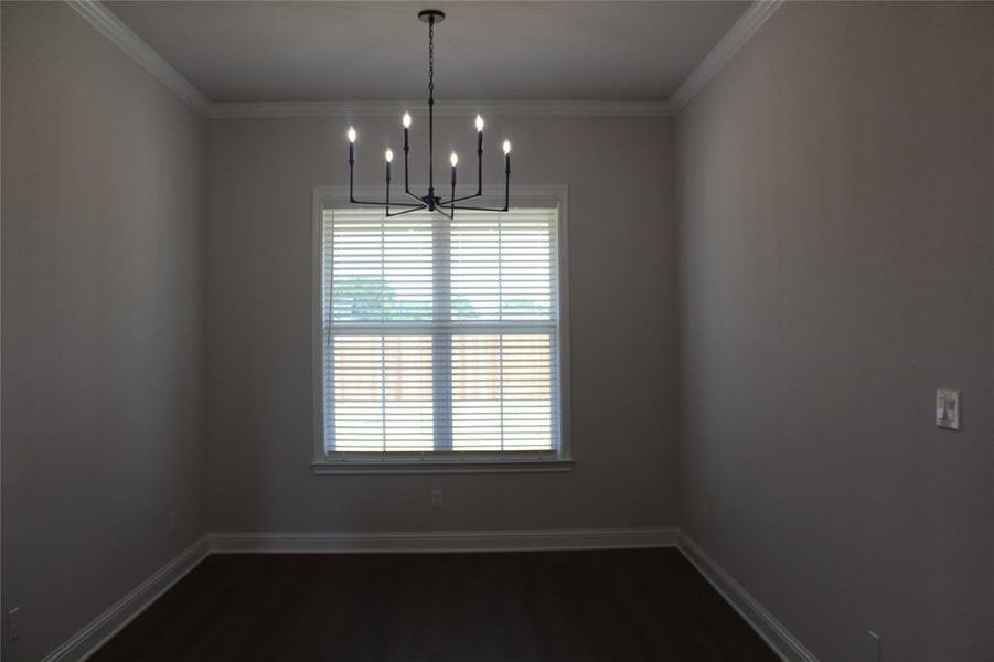 Empty room with a chandelier, dark wood-type flooring, baseboards, and crown molding Empty room with a chandelier, dark wood-type flooring, baseboards, and crown molding