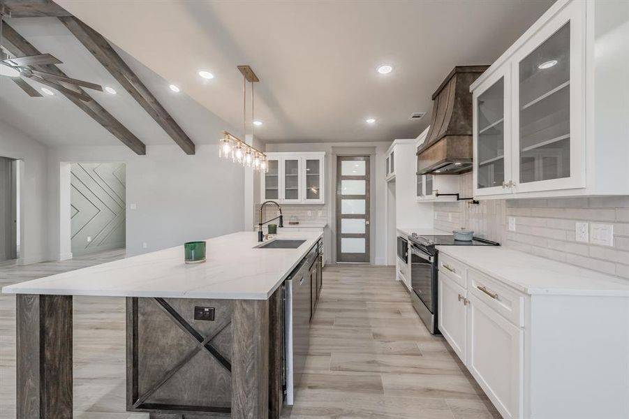 Kitchen with white cabinetry, stainless steel appliances, an island with sink, hanging light fixtures, and glass insert cabinets