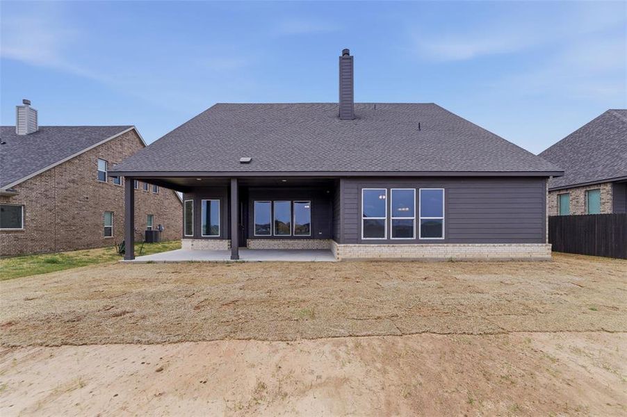 Back of house with a patio area, a chimney, roof with shingles, and brick siding