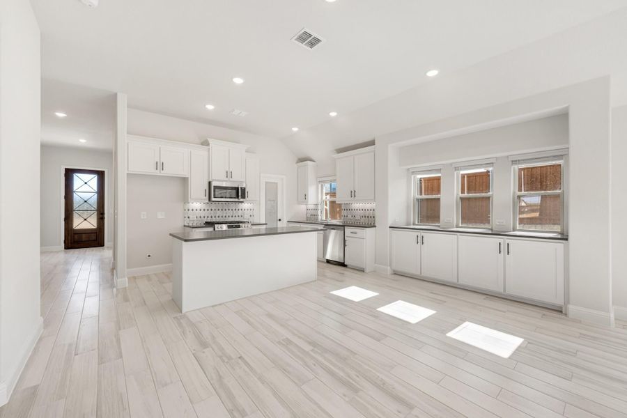 Open kitchen with white cabinets, center island, dark countertops, and light wood-look tile floors