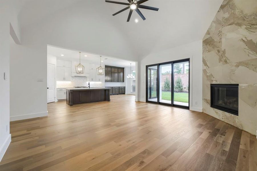 Spacious living area featuring hardwood flooring, a vaulted ceiling with a fan, and a fireplace with a stone surround
