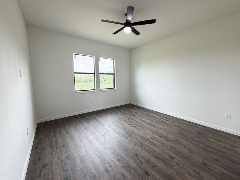 Spacious room featuring wood-finish flooring, white baseboards, and bright white walls Spacious room featuring wood-finish flooring, white baseboards, and bright white walls