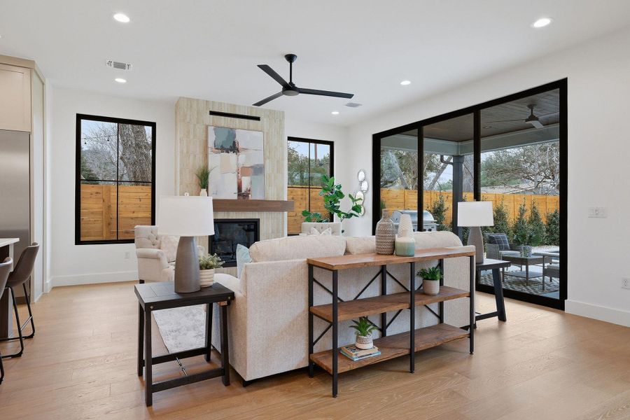 Living area with light wood-type flooring, a tiled fireplace, a ceiling fan, and recessed lighting
