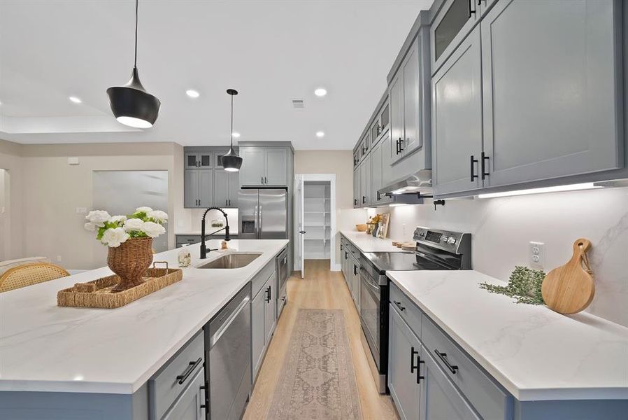 Contemporary kitchen featuring gray shaker cabinetry, light-toned countertops, and wood-finish flooring Contemporary kitchen featuring gray shaker cabinetry, light-toned countertops, and wood-finish flooring