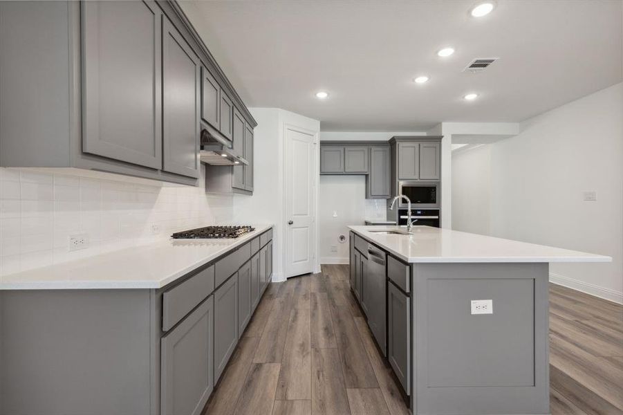 Kitchen featuring gray cabinetry, hardwood / wood-style flooring, decorative backsplash, a center island with sink, and appliances with stainless steel finishes