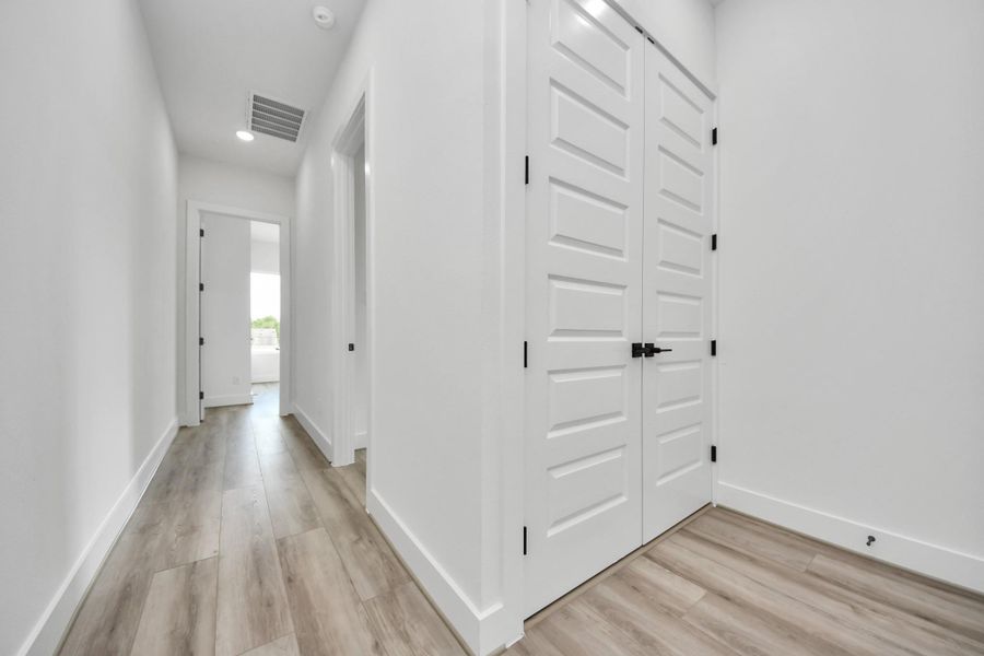 This photo shows a bright, modern hallway with light wood flooring, white walls, and double doors. The space leads to a sunlit room at the end, creating an open and airy feel.