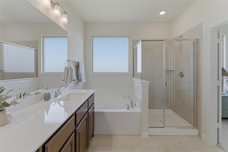 Bathroom featuring a double vanity with an undermount sink, a built-in soaking tub, and a separate glass-enclosed shower with tiled walls
