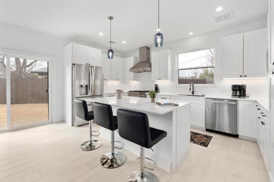 Kitchen with a breakfast bar area, stainless steel appliances, white cabinetry, decorative light fixtures, and light wood-type flooring