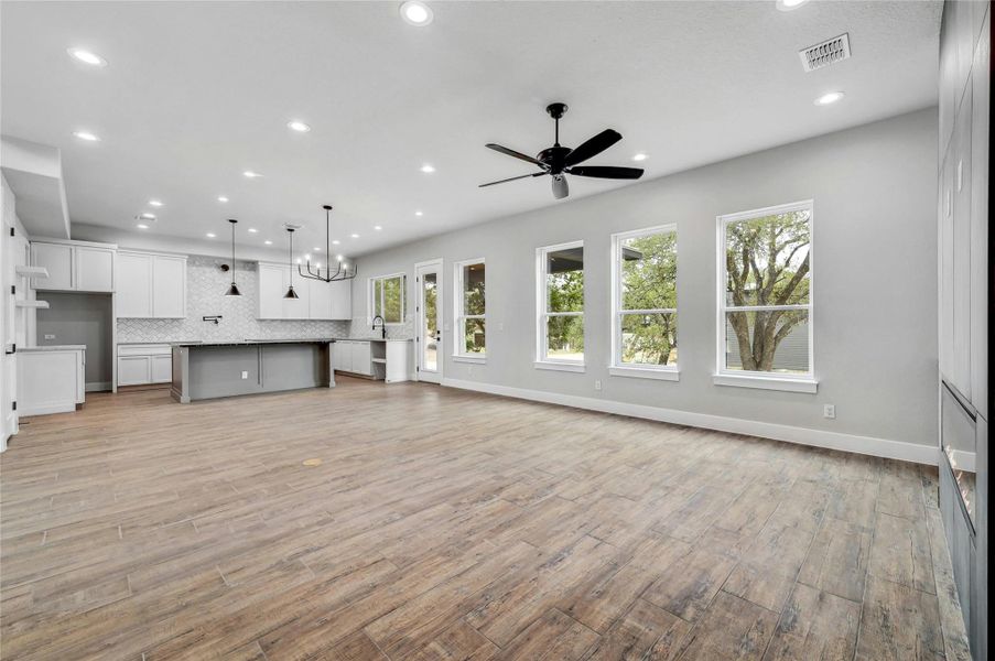 Unfurnished living room with recessed lighting, ceiling fan with notable chandelier, visible vents, baseboards, and light wood-type flooring