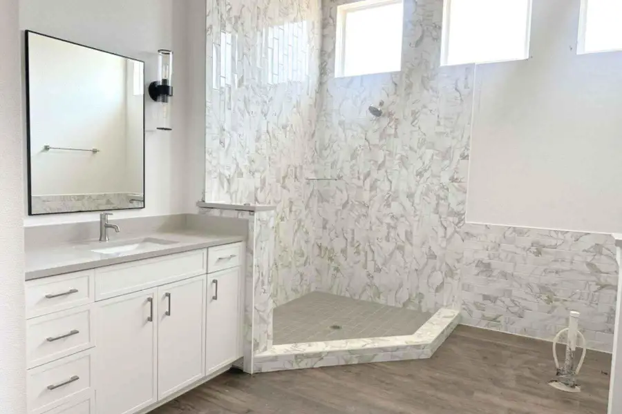 Bathroom featuring vanity, a stall shower, healthy amount of natural light, dark wood-type flooring, and tile walls Bathroom featuring vanity, a stall shower, healthy amount of natural light, dark wood-type flooring, and tile walls