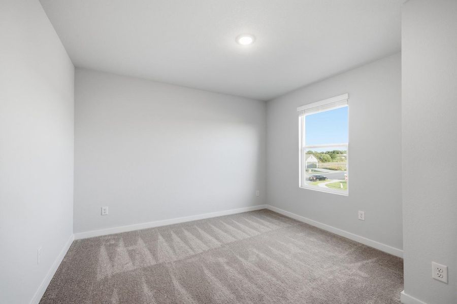 A well-lit bedroom features plush carpeting and an illuminating window providing natural light.