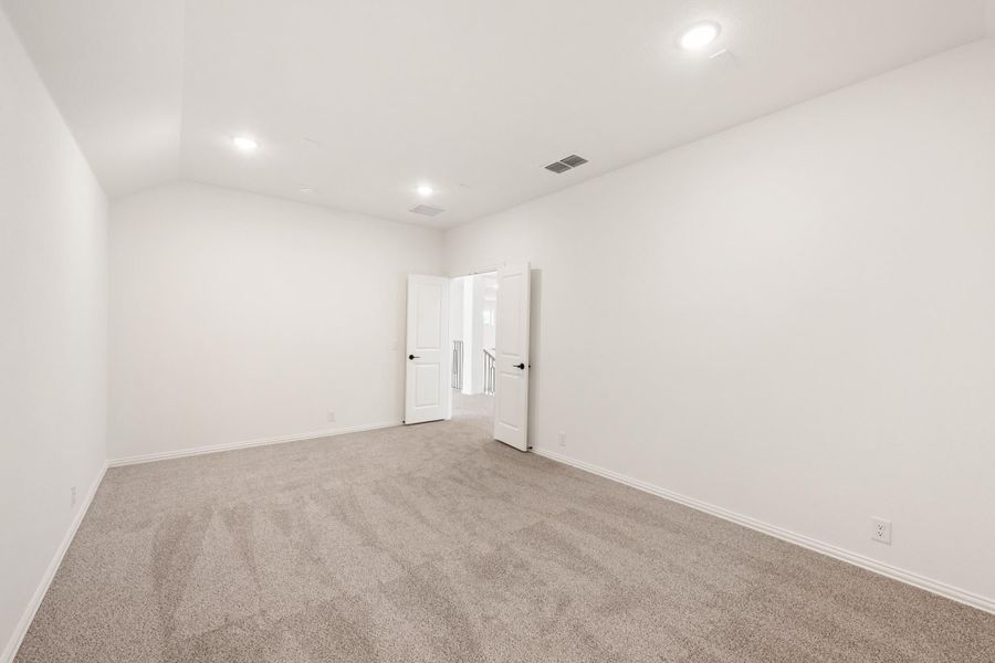 Empty bedroom with white walls, gray carpet, and double doors opening to hallway
