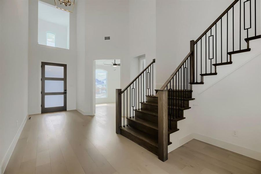 Double-height entry featuring a prominent staircase with dark wood-finish treads and risers, black metal balusters, and a matching handrail Double-height entry featuring a prominent staircase with dark wood-finish treads and risers, black metal balusters, and a matching handrail