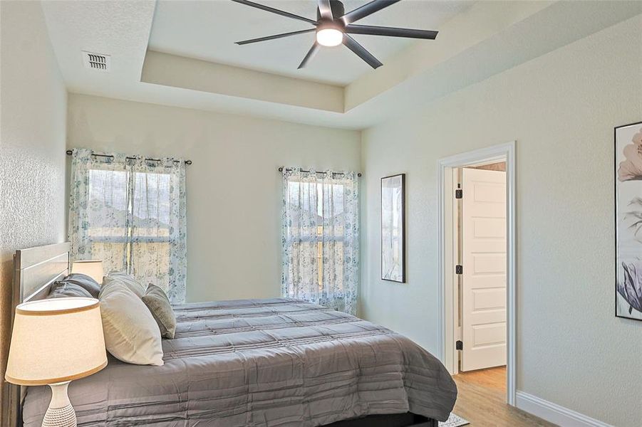 Tray ceiling with a modern ceiling fan, paired with multiple windows featuring decorative curtains Tray ceiling with a modern ceiling fan, paired with multiple windows featuring decorative curtains