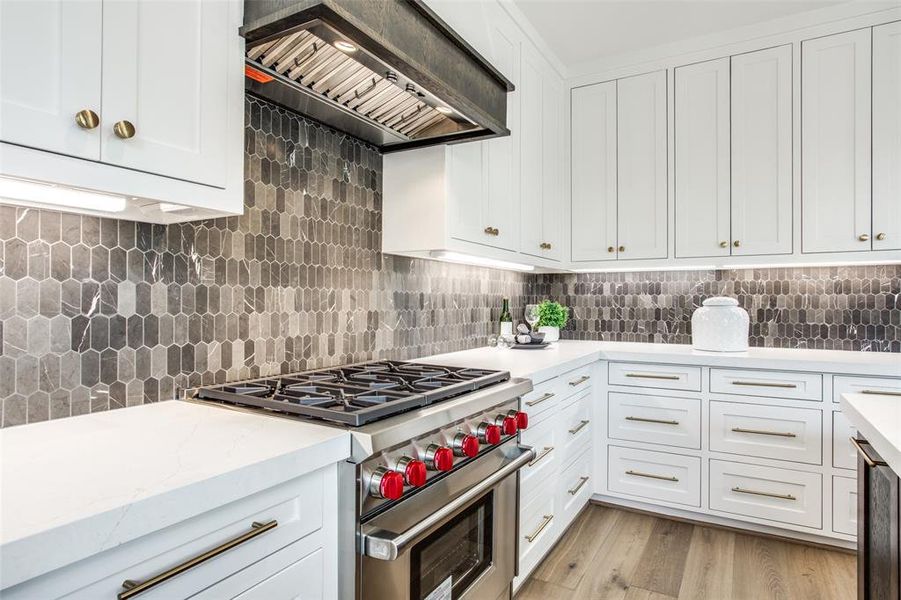 Kitchen with white cabinetry, wolf range hood, light hardwood / wood-style flooring, backsplash, and designer stove