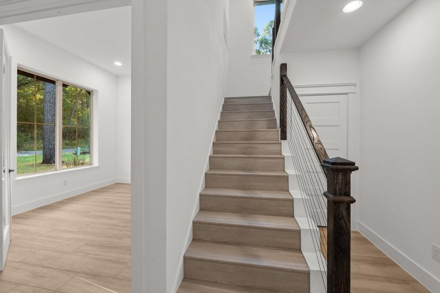 This photo shows a modern, bright entryway with light wood flooring and a staircase featuring a sleek railing. Large windows offer natural light and a view of the greenery outside. This photo shows a modern, bright entryway with light wood flooring and a staircase featuring a sleek railing. Large windows offer natural light and a view of the greenery outside.