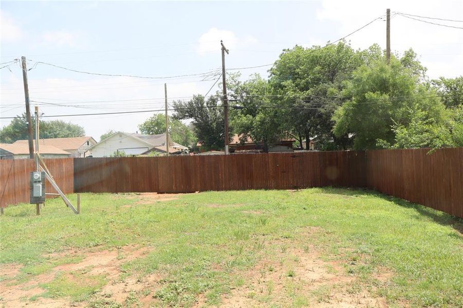Expansive fenced yard featuring a wood privacy fence, grassy area, and mature trees beyond the property line