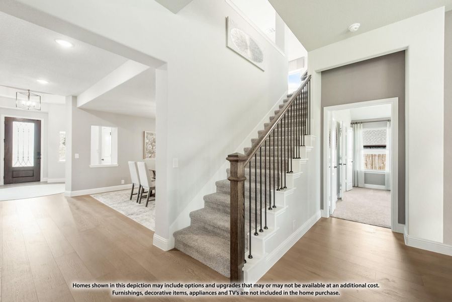 Carpeted staircase with wood railing in open foyer with hardwood floors and front entry door visible Carpeted staircase with wood railing in open foyer with hardwood floors and front entry door visible