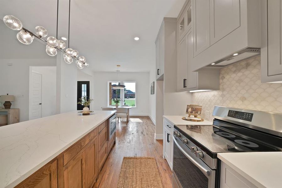 Kitchen featuring stainless steel appliances, light wood-style floors, decorative light fixtures, recessed lighting, and decorative backsplash Kitchen featuring stainless steel appliances, light wood-style floors, decorative light fixtures, recessed lighting, and decorative backsplash