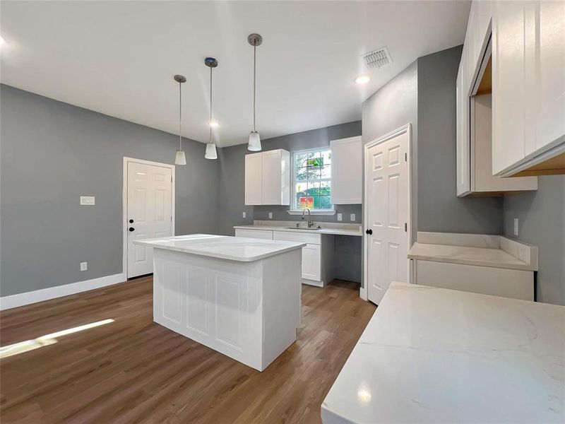 Kitchen with dark wood-type flooring, white cabinets, sink, hanging light fixtures, and a kitchen island